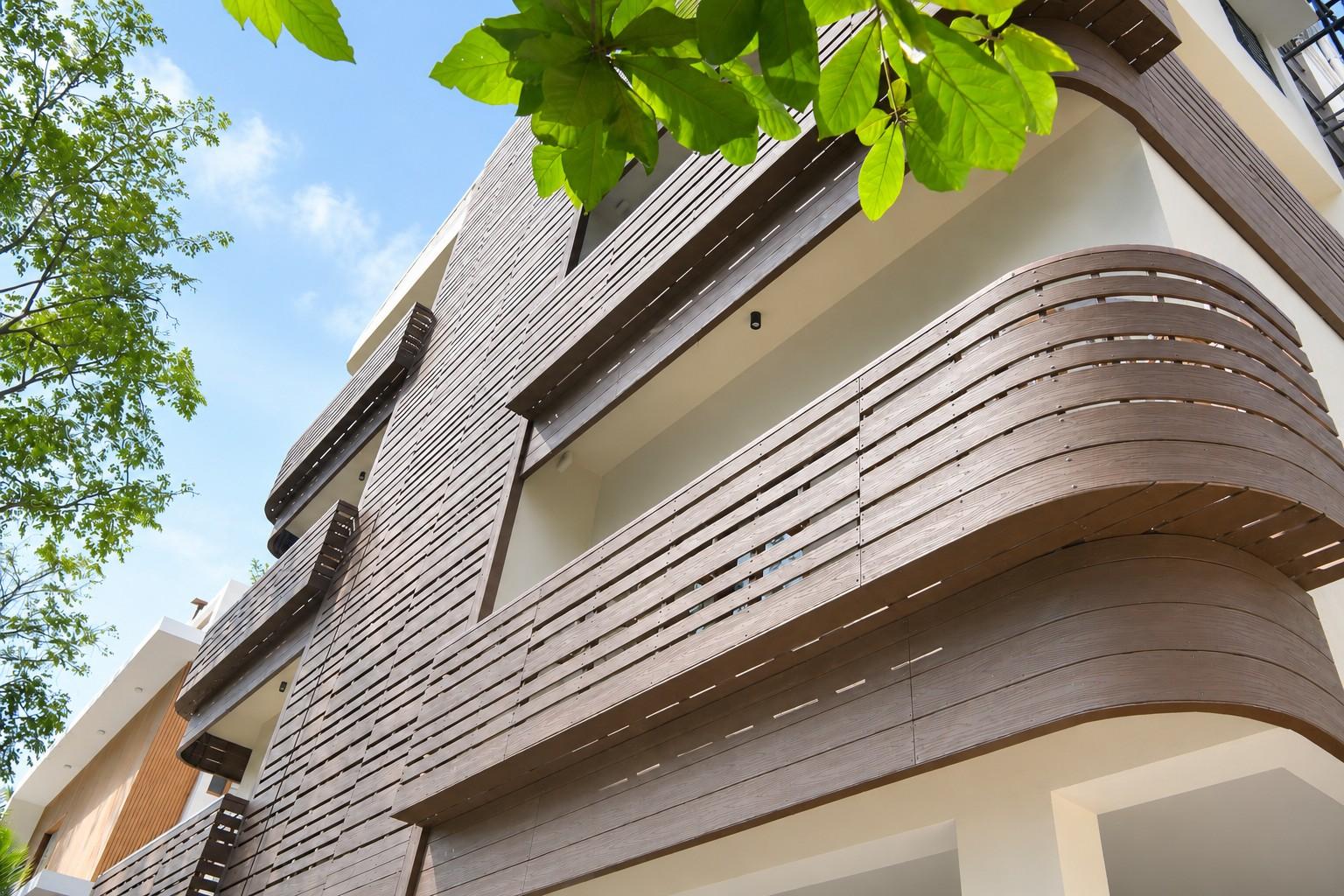 ArchitectsDesigne - Versaplank Modern multi-story building with curved wooden slat balconies, white walls, and green trees overhead against a blue sky.