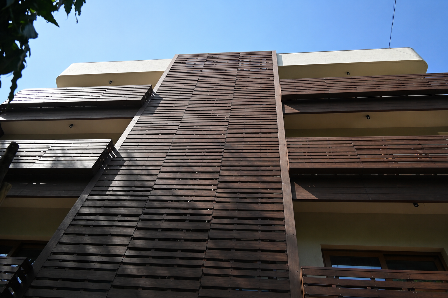 Fabricators - Versaplank Low-angle view of a modern apartment building with dark wooden slat panels and balconies against a clear blue sky.