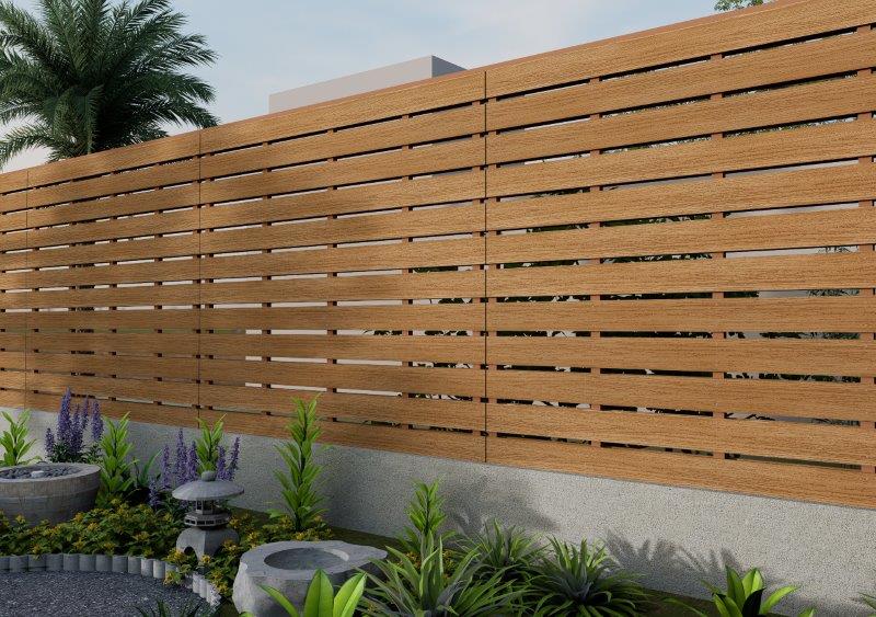Horizontal wooden slat privacy fence with a concrete base, in a landscaped backyard with green plants and purple flowers in planters.